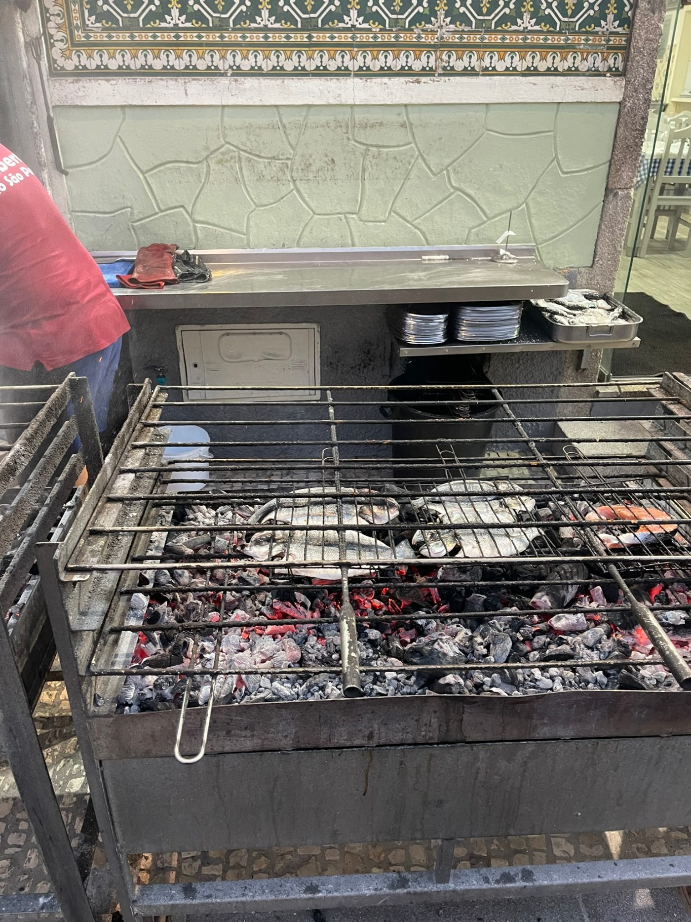 Whole fish grilling over glowing charcoal in an outdoor brazier